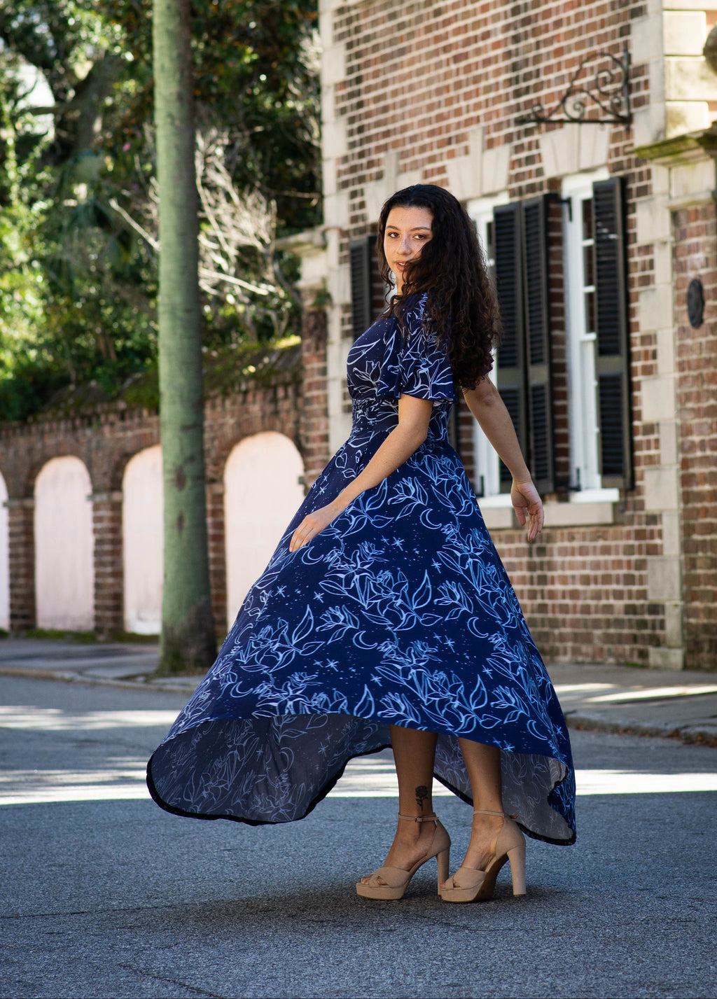 Woman in a blue floral Sarah Camille Art dress standing on a Charleston SC street with a brick building in the background